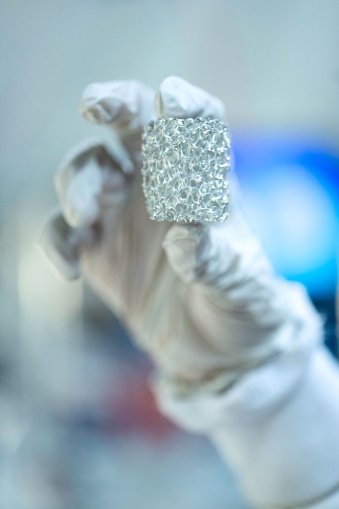Close-up of a scientist holding metallic foam in a lab setting, highlighting innovation.